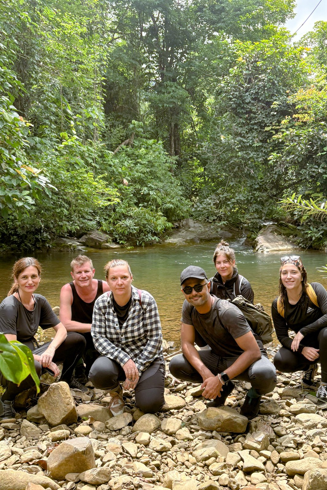 A group of seven travellers crouching by the freshwater pool, surrounded by jungle, after the trek