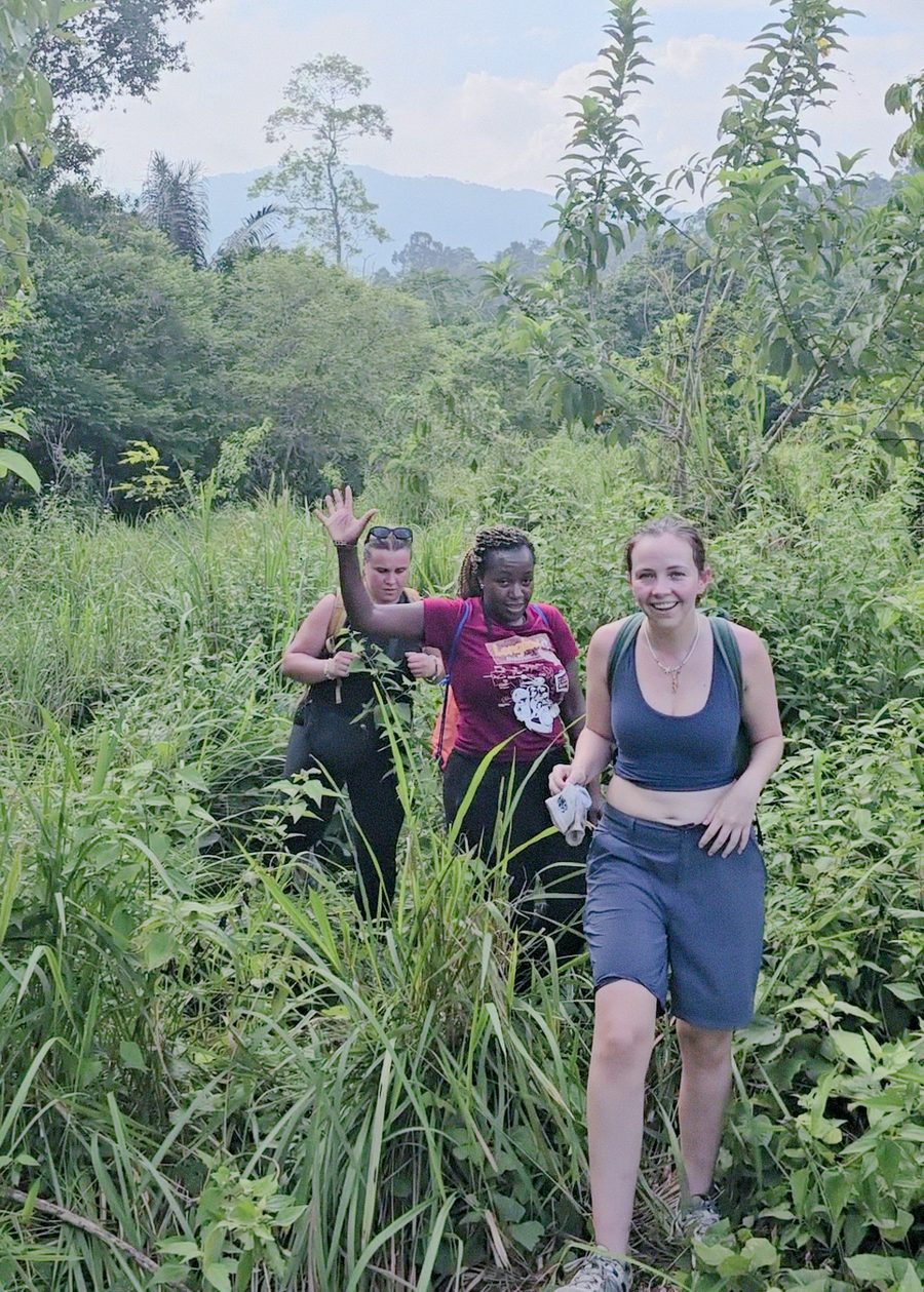 Three trekkers wading across a fast-flowing jungle stream with backpacks held high