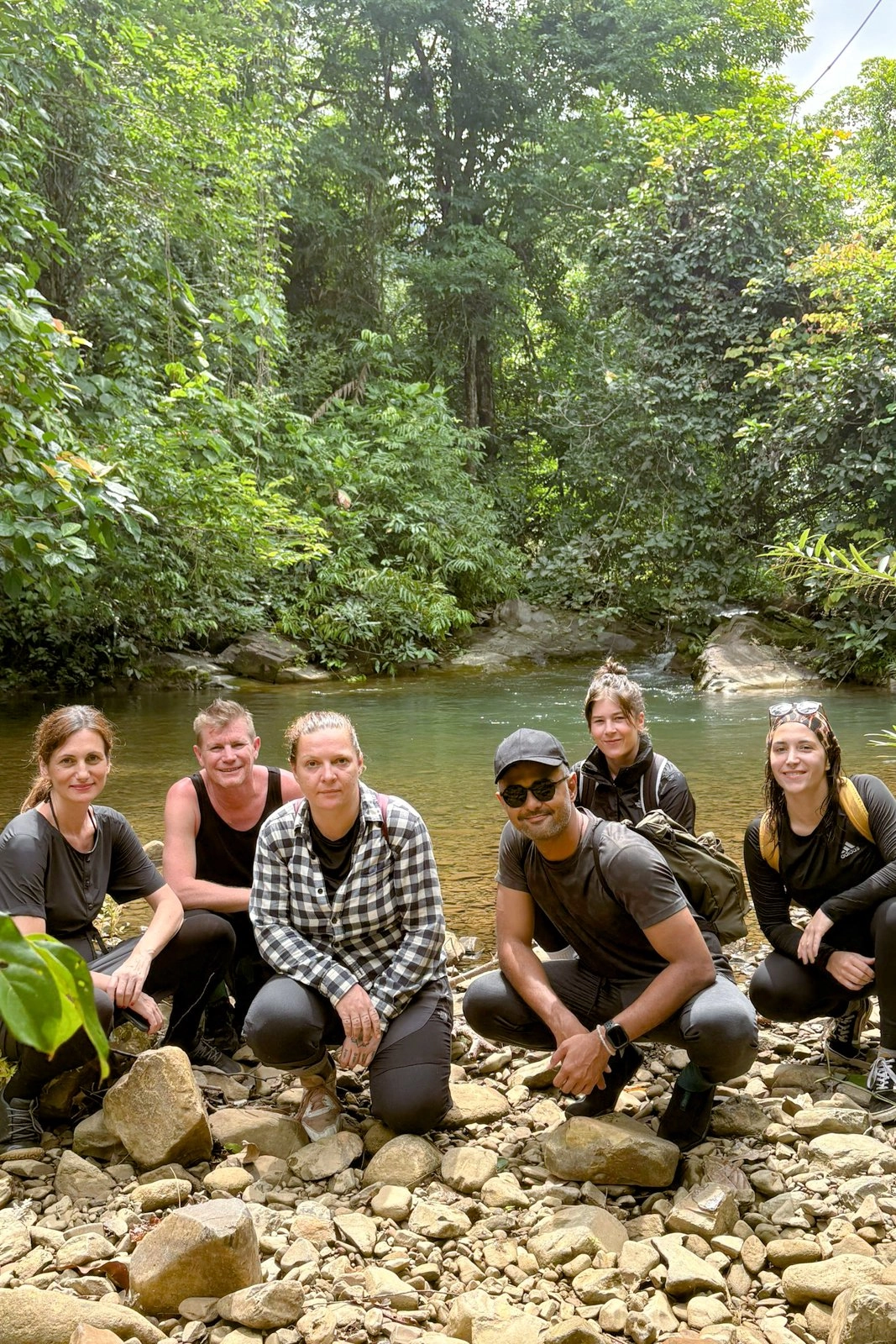 A group of seven travellers crouching by the freshwater pool, surrounded by jungle, after the trek