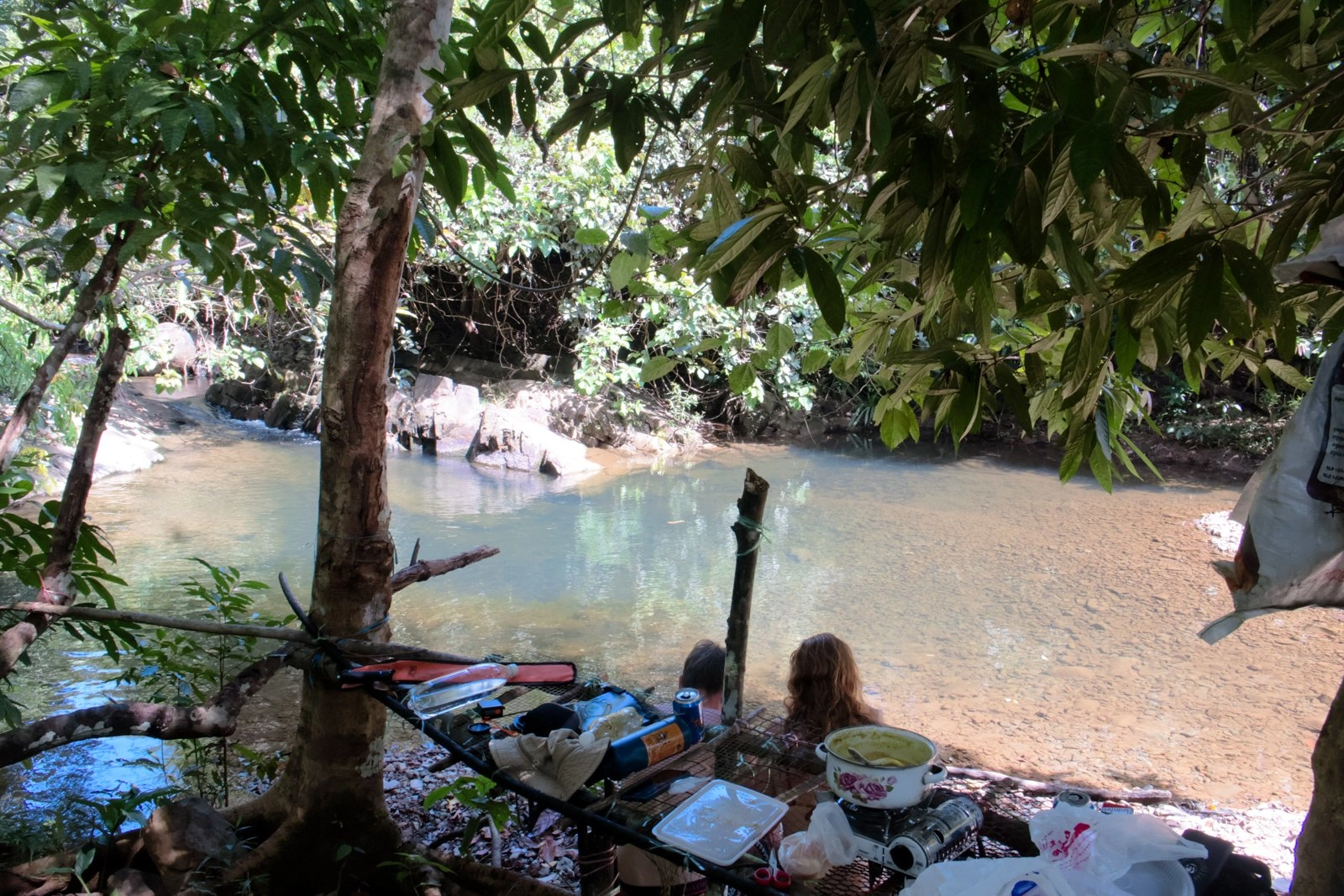 The Jungle Bar — handmade table by the water with cooking pot and view of the freshwater pool