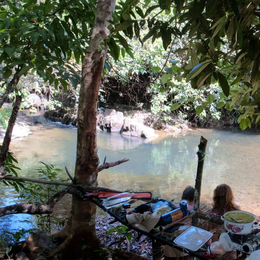Friends eating freshly cooked lunch by the rocky pond